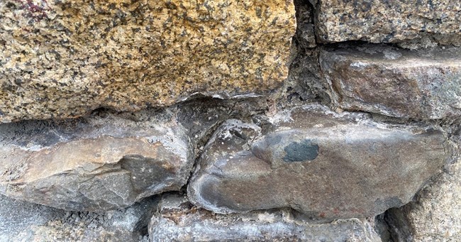 A close-up of multi-colored stones with the mortar chipped out from between the joints.