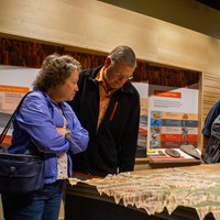 A couple stands among other people examining a relief map within the park museum