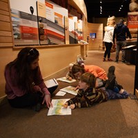 Three children and an adult sit on the floor working on an activity book