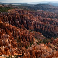 A vibrant landscape of red and white limestone rock spires stand in rows among trees and steep cliff