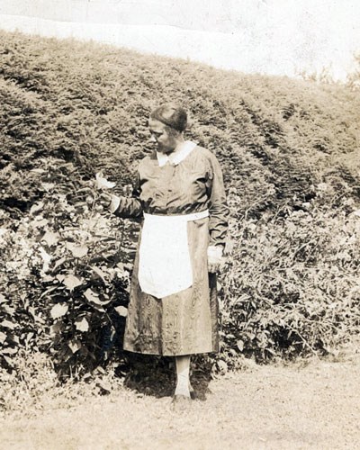 Lizzie McDuffie in a maid's dress with apron in a garden.