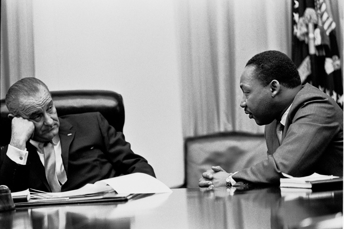 President Lyndon B Johnson and Dr. Martin Luther King Junior seated at a table in discussion.
