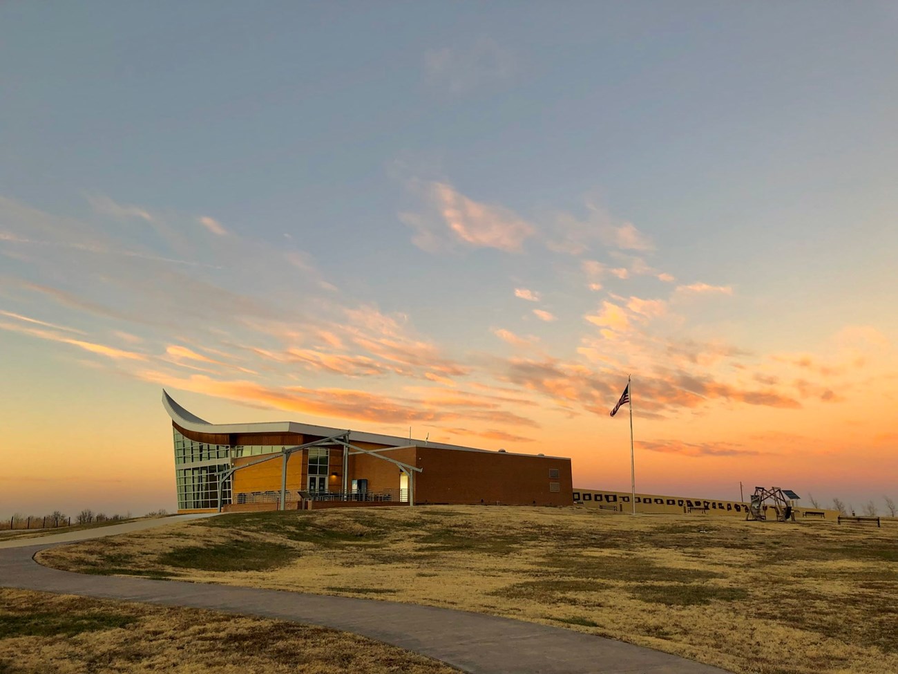 The plow shaped visitor center is in the foreground. A pale pink sky can be seen behind it as the sunsets.