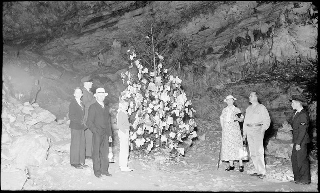 A black and white photo of people standing around a Christmas Tree in a cave