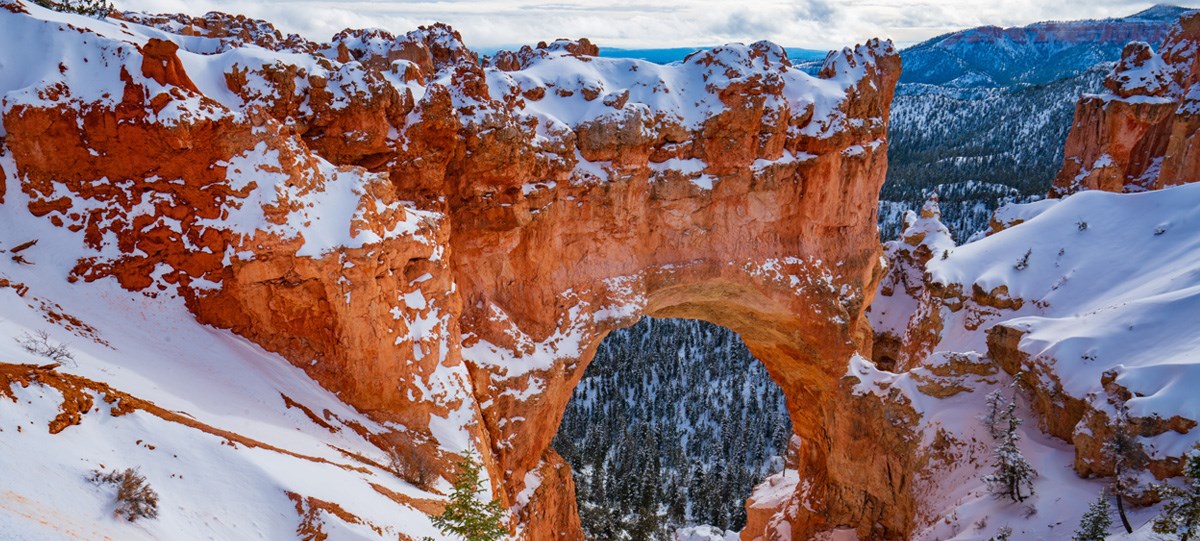 A red rock formation in the shape of an arch covered in snow.