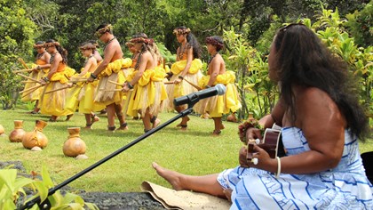 Woman singing to a line of hula dancers