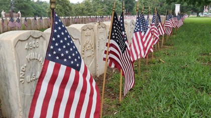 A line of national cemetery headstones lined with planted US flags