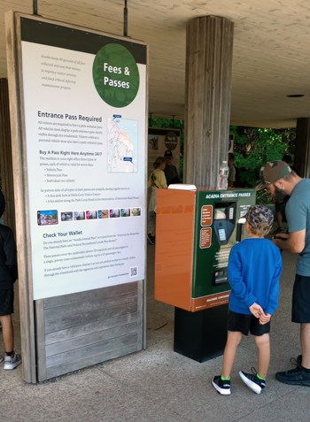 A man and boy interact with a fee machine next to a large interpretive panel
