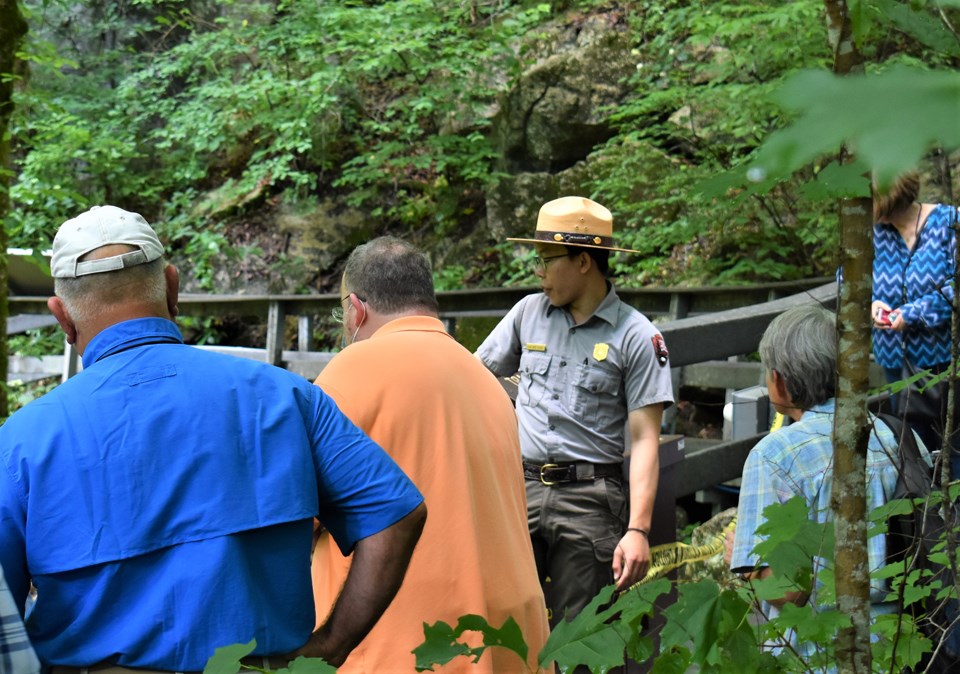 A male ranger points over a gray boardwalk as a group of visitors watch on.