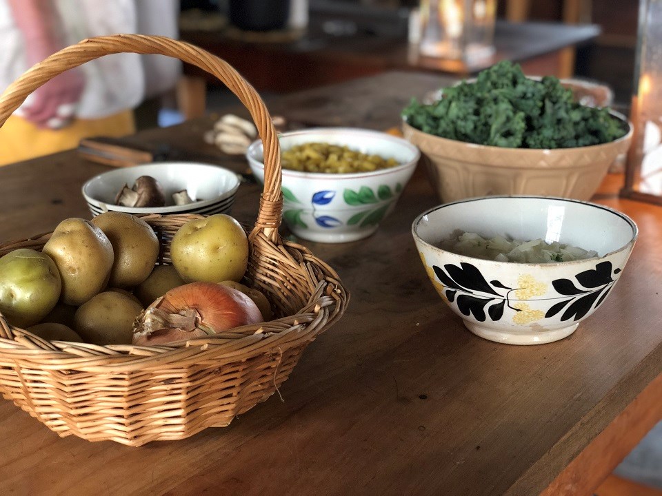 Potatoes, onions, and other ingredients in baskets and bowls on a table.