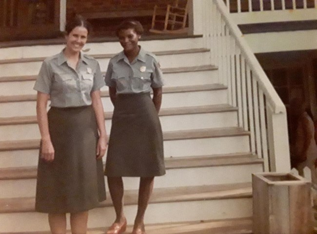 Anne Jordan and Judy Forte pose in the NPS uniforms standing on wooden stairs in front of a building.