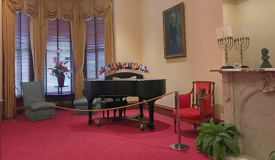 Parlor with a piano, red carpet, fireplace, chandelier, and painting of Mary McLeod Bethune