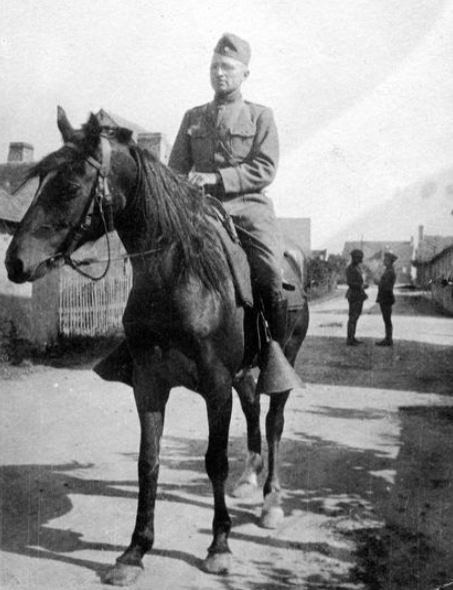 Harry Truman, in military uniform, rides a horse on a village street.