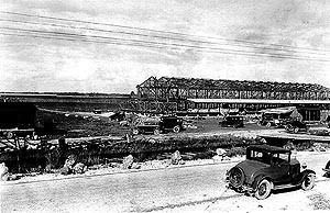 The H.W. Bird Tomato Corporation packing facility, along Birdon Road. Black and white images featuring an antique car parked on a dirt road overlooking the skeletal structure of a packing facility.