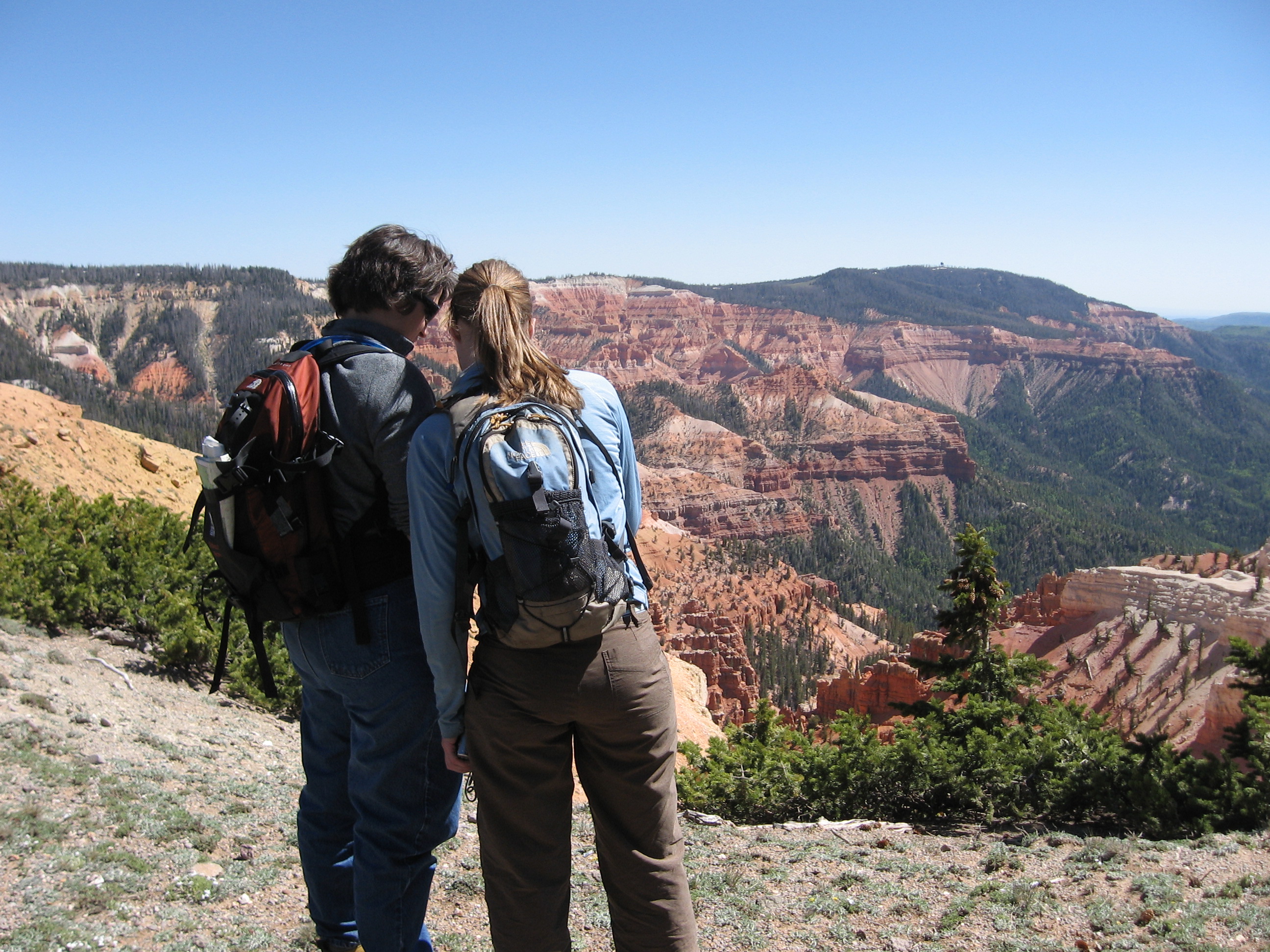 Two hikers standing at overlook of Cedar Breaks on clear, sunny day