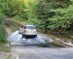 A car drives through a water where the road dips down into a low area.
