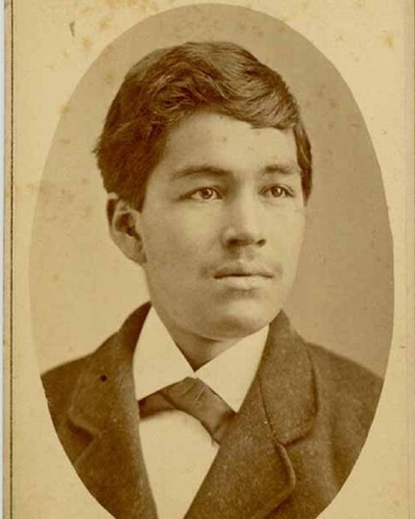 Sepia toned image of a young man in a suit and bow tie in an oval shape inset in paper
