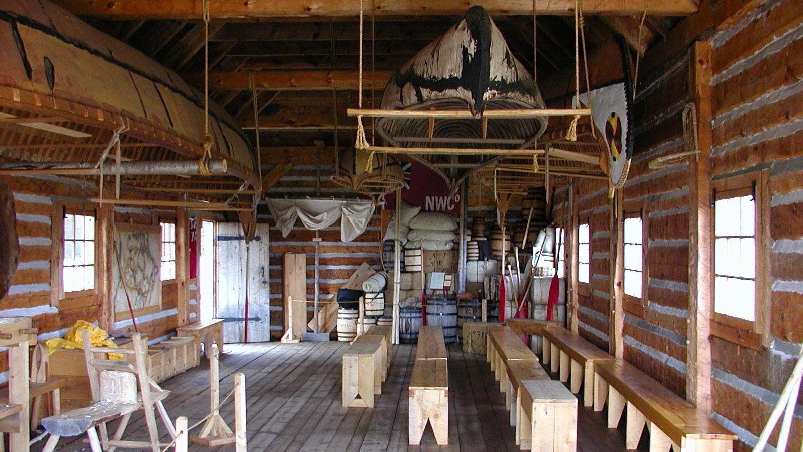 Inside of a historic wood building with rows of benches and canoes hanging from the rafters.