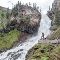 A hiker stands at the base of a large waterfall.