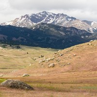 A rocky mountain peak emerges behind rolling, grassy hills.
