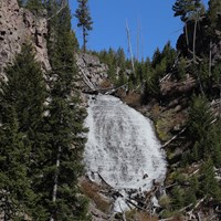 Water cascades down a slope surrounded by rocky cliffs and sparse trees.