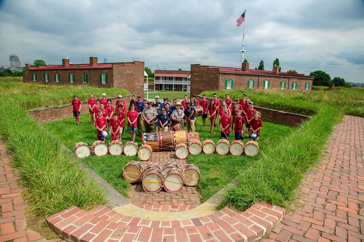 Fife and drum camp students on bastion with flag in background