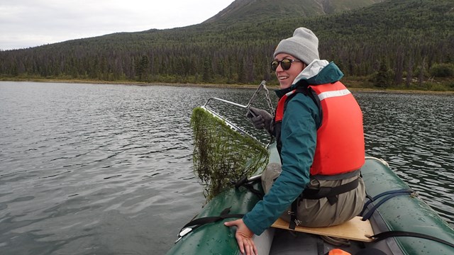 Woman riding in a canoe, displaying green algae pulled from the lake