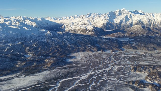 An aerial shot of a snow-capped mountain ranger with braided river running through the valley below.
