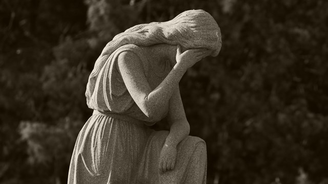 A stone woman kneeling with her face lowered in one hand.