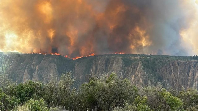Fire and smoke filling the sky along the far rim of a canyon