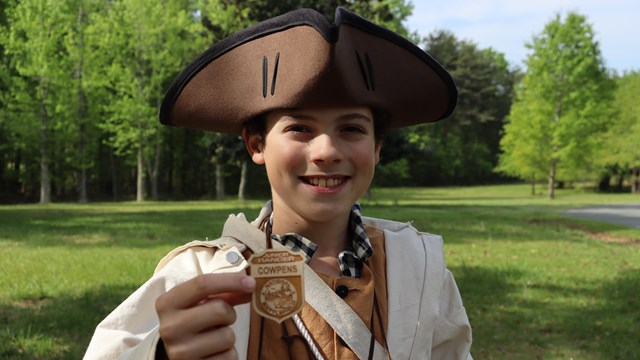 Visitor dressed as a militia soldier holds a Junior Ranger badge