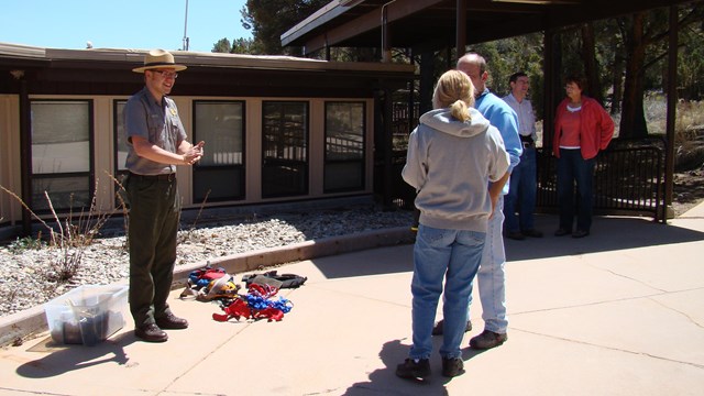Three people talking one is in a park ranger uniform of green and grey. They are standing in the sun