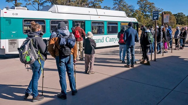 a line of people wearing winter clothing about to board a green and white bus at a bus stop