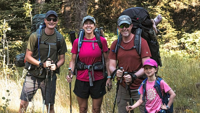 A group of three adults and one child poses for a photo with their backpacking packs on.