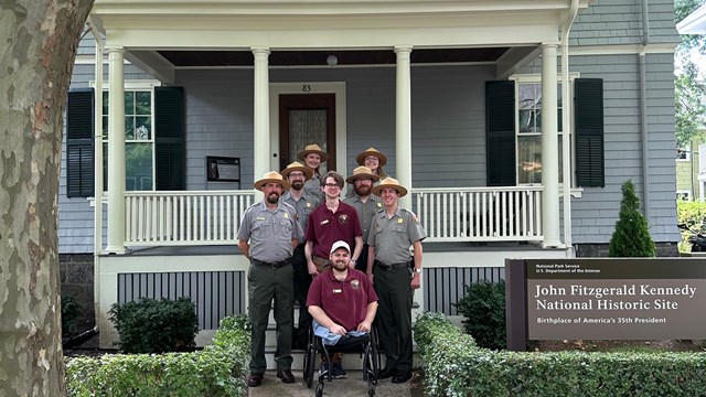 Photograph of 2024 season staff in front of JFK birthplace home with tree and sign in foreground.