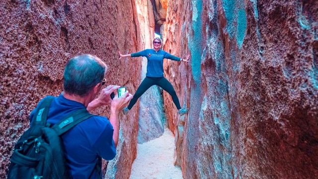 A woman poses for a photo and braces against the sides of a slot canyon.