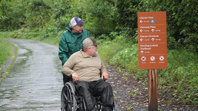 Two people, one in a wheelchair, look at trail signage