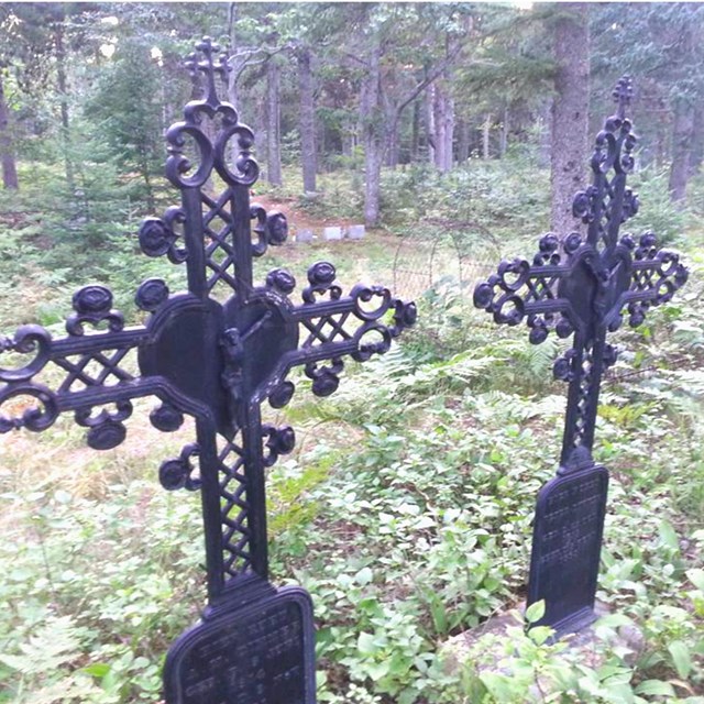 Two cast iron grave markers stand next to each other in a cemetery.