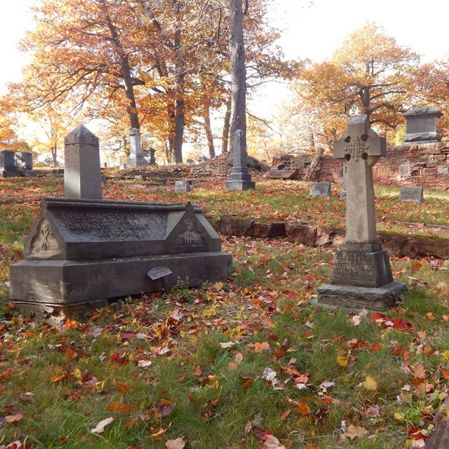 Two grave markers are surrounded by a short masonry fence in a cemetery.