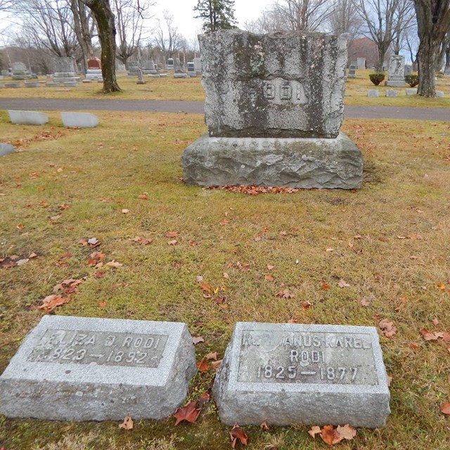Two small grave markers are in front of a large family grave marker labeled 