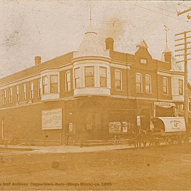 A building is situated on a street corner intersection, with a horse drawn carriage out front.