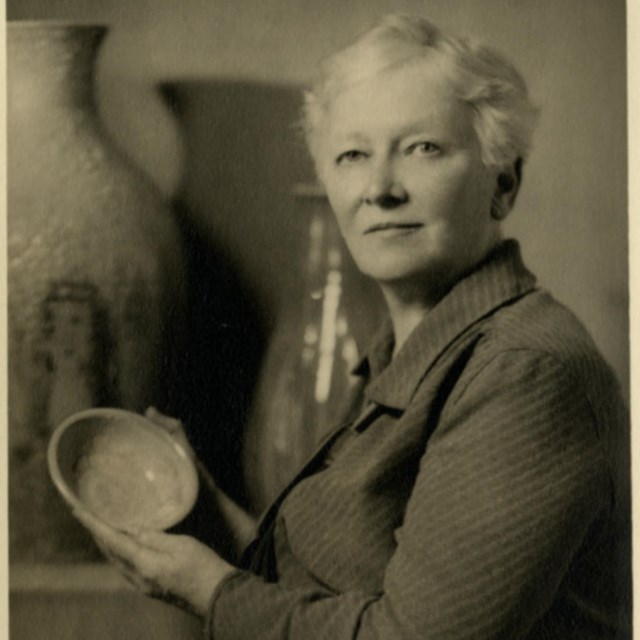 A woman looks at a camera to pose for a photograph while holding a bowl up.