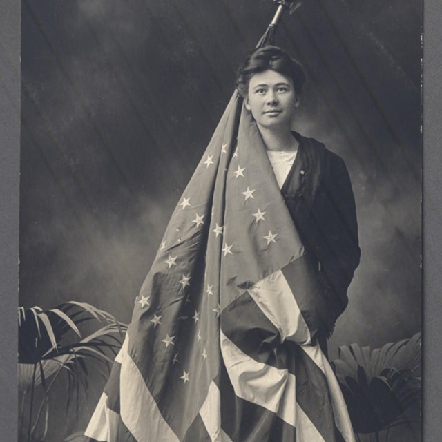 A women poses for a photograph holding an American flag that is draped around her body.