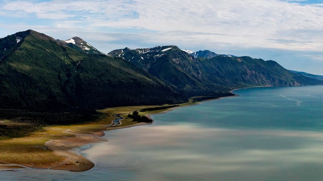 Two-toned water meets an uneven shore with rivers disappearing into forest and up into mountains.