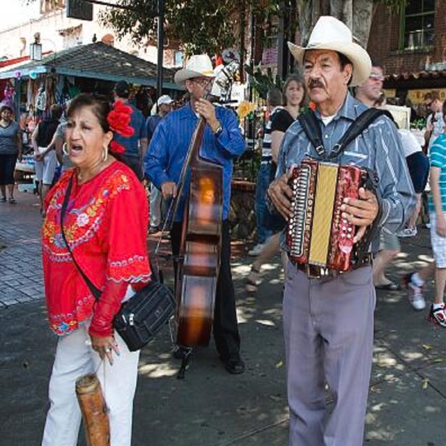 Four street musicians playing music on Olvera Street while people walk in the background