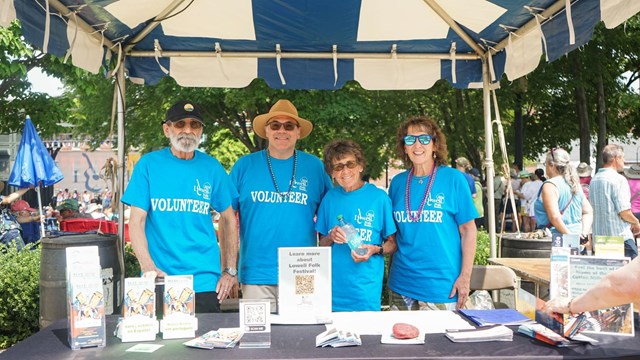 Four people wearing bright blue volunteer shirts stand behind an information table