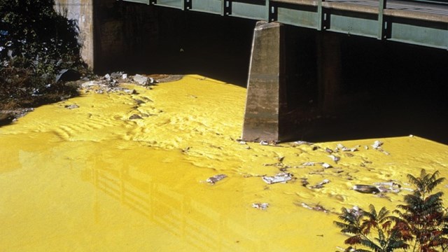 The Nashua River is an unnatural, bright yellow as it flows under a bridge, and is filled with dye