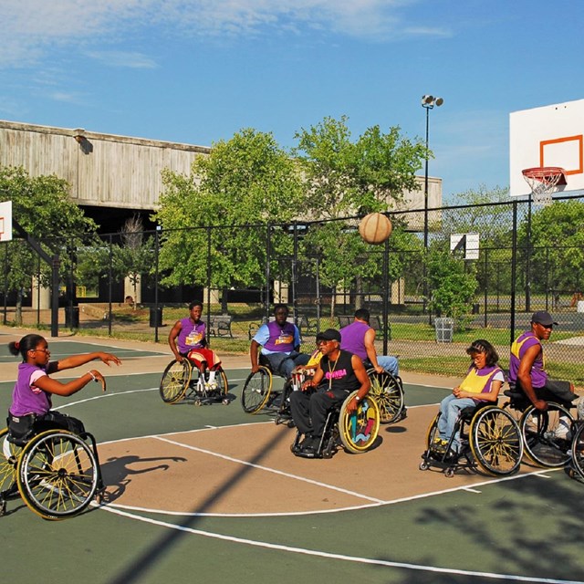 Group in wheelchairs playing basketball on an outdoor court