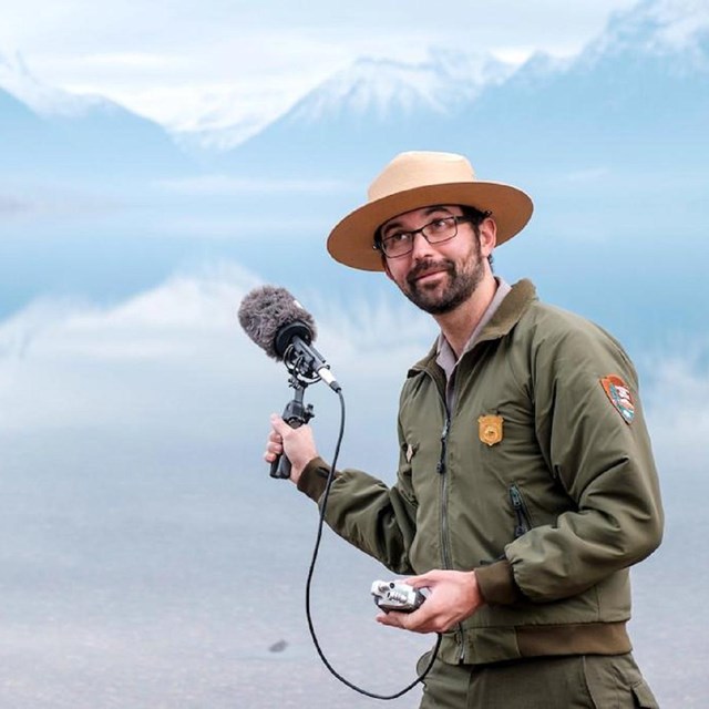 Park ranger holding a recording microphone in front of a lake and mountains