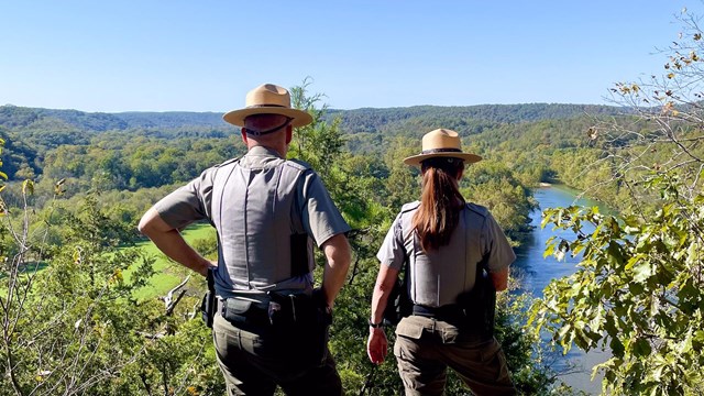 Two park rangers overlook the river from a cliff.